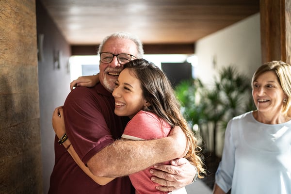 Older man standing next to his wife hugs daughter