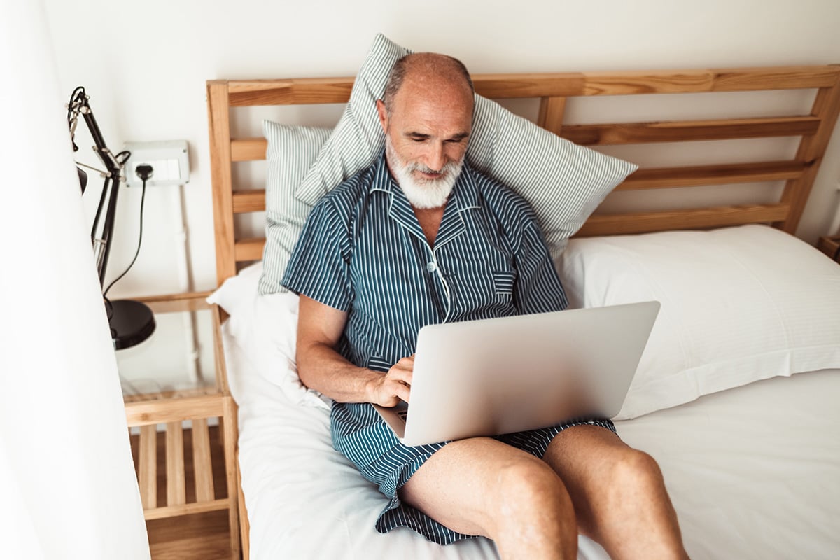 Senior man in pajamas in bed looking at laptop
