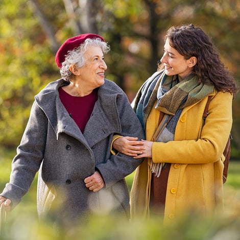 Senior woman and daughter wearing jackets walk arm in arm on path