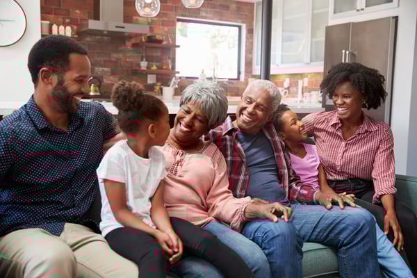 grandparents, parents, and children sitting on a couch and laughing at eachother