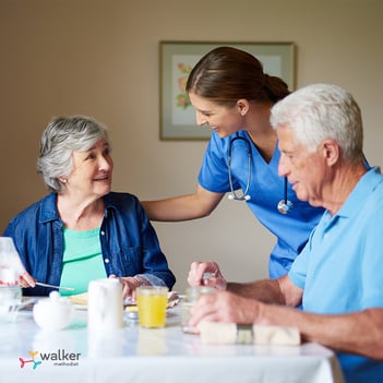 Senior facility staff talks with man and woman at dining table