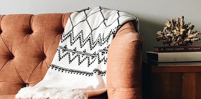 Blanket drapes against back of tufted sofa next to end table