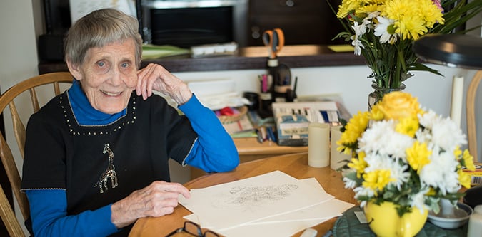 Elderly woman sitting at table drawing